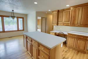 Kitchen with light countertops, baseboards, a kitchen island, and light wood flooring