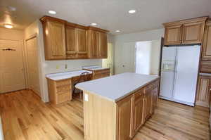 Kitchen featuring a center island, white refrigerator with ice dispenser, light countertops, light wood finished floors, and recessed lighting