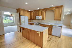 Kitchen with a sink, light countertops, light wood-style floors, recessed lighting, and white appliances