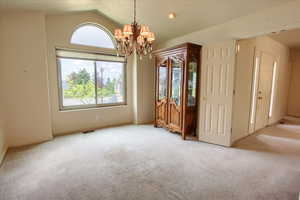 Dining room with carpet flooring, a chandelier, a wealth of natural light, and vaulted ceiling