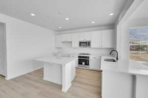 Kitchen featuring recessed lighting, light wood-type flooring, white cabinetry, a sink, and appliances with stainless steel finishes