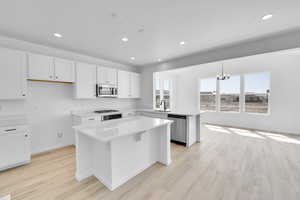 Kitchen featuring a kitchen island, light wood-type flooring, light countertops, an inviting chandelier, and stainless steel appliances