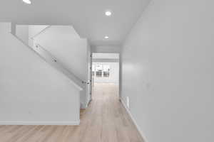 Hallway featuring recessed lighting, light wood-style flooring, baseboards, and stairway