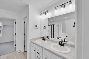 Bathroom with double vanity, a sink, wood finished floors, and a shower stall