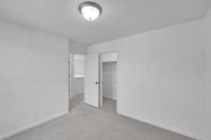 Unfurnished bedroom featuring baseboards, light colored carpet, a spacious closet, and a closet