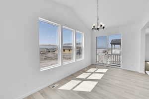 Unfurnished dining area featuring an inviting chandelier, visible vents, baseboards, wood finished floors, and vaulted ceiling