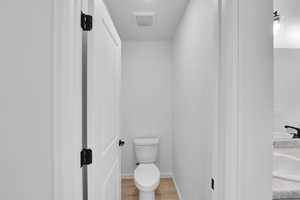 Bathroom featuring a sink, toilet, baseboards, wood finished floors, and visible vents