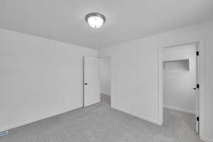Unfurnished bedroom featuring baseboards, carpet, a walk in closet, and visible vents