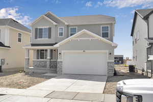 View of front of property with stone siding, stucco siding, central AC unit, an attached garage, and driveway