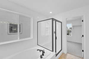 Bathroom featuring baseboards, a shower stall, wood finished floors, and a garden tub
