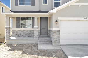 Property entrance featuring covered porch, an attached garage, a shingled roof, stone siding, and stucco siding