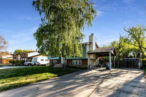 Split level home with a front lawn, fence, a chimney, brick siding, and driveway