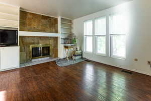 Unfurnished living room with a textured ceiling, a stone fireplace, built in features, visible vents, and hardwood / wood-style flooring