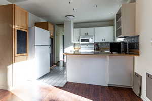 Kitchen featuring open shelves, white appliances, a peninsula, decorative backsplash, and wood finished floors