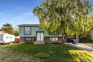 Raised ranch featuring fence, a front yard, brick siding, board and batten siding, and driveway