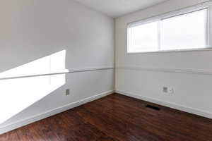 Spare room featuring visible vents, baseboards, and wood finished floors