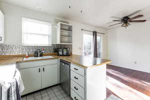 Kitchen featuring decorative backsplash, ceiling fan, stainless steel dishwasher, a sink, and a peninsula