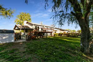 Back of house with a lawn, a deck, an outbuilding, stairway, and a storage unit