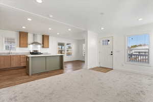 Kitchen featuring wall chimney range hood, stainless steel range, recessed lighting, baseboards, and a kitchen island