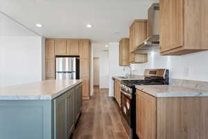 Kitchen with wall chimney range hood, appliances with stainless steel finishes, a sink, light countertops, and wood finished floors