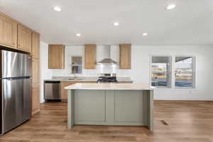 Kitchen with wall chimney range hood, appliances with stainless steel finishes, recessed lighting, baseboards, and a kitchen island