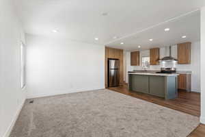 Kitchen featuring a kitchen island, appliances with stainless steel finishes, light countertops, baseboards, and wall chimney exhaust hood