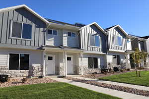View of property featuring board and batten siding, central AC, stone siding, and a front lawn
