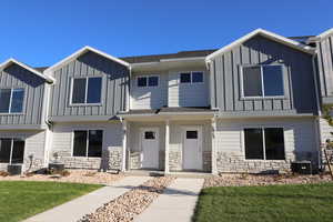 Townhome / multi-family property with a front lawn, board and batten siding, stone siding, and cooling unit