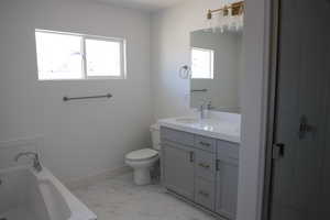 Bathroom featuring vanity, toilet, marble finish floor, a tub, and baseboards