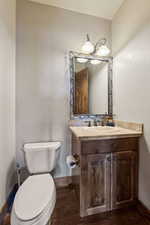 Half bathroom with vanity, baseboards, wood finished floors, and toilet
