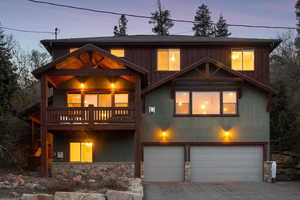 View of front of home with stone siding, a garage, stucco siding, concrete driveway, and a balcony