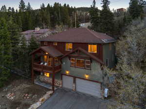 Rustic home featuring a forest view, roof with shingles, aphalt driveway, an attached garage, and stone siding