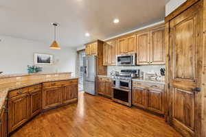 Kitchen with pendant lighting, appliances with stainless steel finishes, light stone countertops, brown cabinets, and wood finished floors