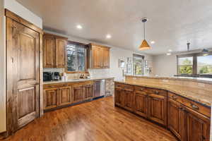 Kitchen with light stone counters, a sink, recessed lighting, wood finished floors, and stainless steel dishwasher