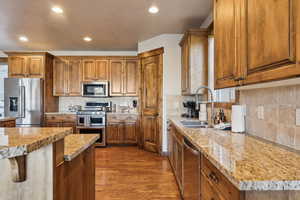 Kitchen featuring appliances with stainless steel finishes, a sink, brown cabinetry, decorative backsplash, and dark wood-style floors