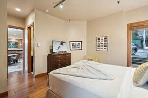 Bedroom with track lighting, access to exterior, wood finished floors, and baseboards