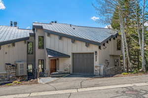 View of front of home featuring a garage, a standing seam roof, aphalt driveway, and stone siding