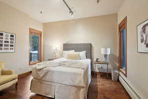 Bedroom with track lighting, baseboards, baseboard heating, dark wood finished floors, and a baseboard heating unit