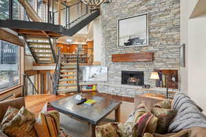 Living area with a fireplace, a high ceiling, stairs, a baseboard radiator, and wood finished floors