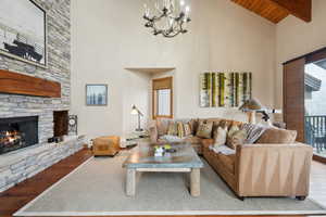 Living room featuring beam ceiling, a stone fireplace, high vaulted ceiling, and wood finished floors