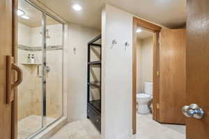 Full bath with tile patterned floors, toilet, a stall shower, and baseboards