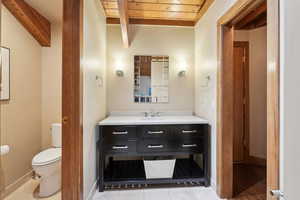 Bathroom featuring toilet, vanity, baseboards, and beam ceiling