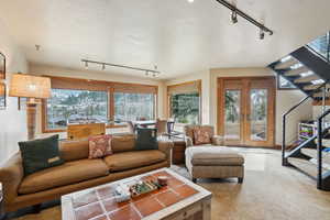 Carpeted living area with stairway, french doors, and a textured ceiling