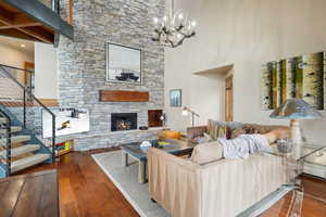 Living area featuring a towering ceiling, a stone fireplace, a chandelier, stairs, and wood-type flooring