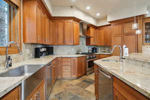 Kitchen with stainless steel appliances, brown cabinetry, wall chimney exhaust hood, and a sink