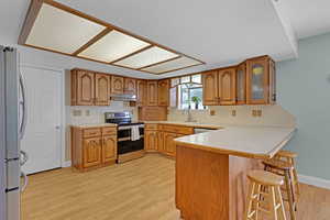 Kitchen featuring brown cabinetry, a peninsula, light wood-style floors, under cabinet range hood, and stainless steel appliances