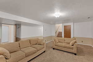 Living area featuring carpet floors, baseboards, stairs, and a textured ceiling