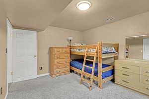 Carpeted bedroom featuring a textured ceiling, visible vents, and baseboards