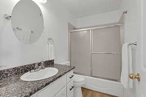 Full bathroom with toilet, enclosed tub / shower combo, wood finished floors, and vanity