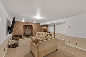 Carpeted living room featuring a textured ceiling, baseboards, a wood stove, and brick wall